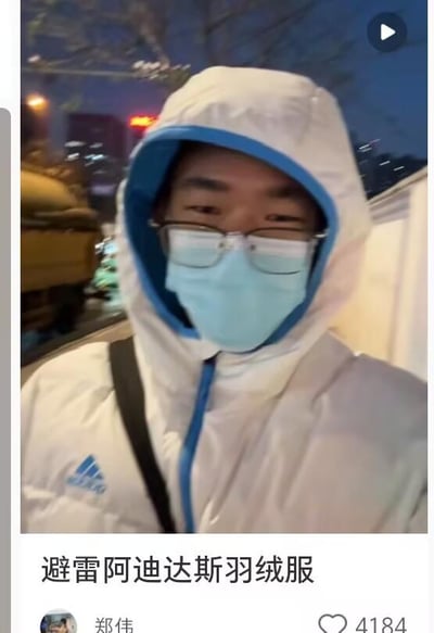 夜晚街头场景中，一名男子身着白色阿迪达斯连帽羽绒服，内搭蓝色内衬，佩戴眼镜和浅蓝色口罩，连帽拉起遮挡头部。图片下方有用户“郑伟”发布的文字“避雷阿迪达斯羽绒服”，疑似针对该羽绒服的质量、保暖性或设计问题进行吐槽。背景可见模糊的城市夜景灯光、车辆及建筑物轮廓，整体氛围为真实的户外拍摄环境。