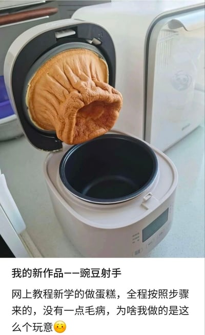 整张图为图文混排的实拍静态图，上半部分展示了一台开盖的家用电饭煲，电饭煲内胆中空无一物，而锅盖内侧的加热面粘连了一整块完全脱离内胆的棕褐色蛋糕，蛋糕膨胀后呈中空褶皱的筒状，向外突出的外形酷似游戏《植物大战僵尸》中的植物角色豌豆射手；图片下半部分是发布者配文，称自己跟着网上教程学做电饭煲蛋糕，全程严格遵循步骤操作，却做出了这样的成品，调侃该成品是自己的“新作品——豌豆射手”，末尾搭配了一个困惑的小黄脸表情，吐槽自己的做饭翻车经历。