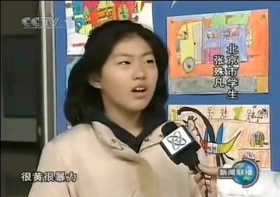 这是央视《新闻联播》的一段采访视频截图，画面中的人物是北京市学生张殊凡，她正对着带有央视标志的话筒接受采访，背景是贴有儿童画作的蓝色墙面。画面右侧标注了她的身份“北京市学生 张殊凡”，左下角配有她的发言字幕“很黄很暴力”。这句话在当时成为了广为流传的网络热词，相关截图被网友在各大网络社区用于玩梗。