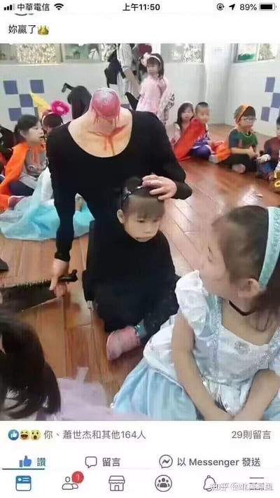 图片显示一个室内儿童活动场所，多名穿着各色服装的儿童围坐四周。画面中央有一个无头人士，颈部有红色类似血迹的物质，身穿黑色衣服，手持刀具跪坐在地，正在触摸一名小女孩的头部。图片顶部有“妳赢了👑”的文字，整体场景令人感到不安和惊悚。
