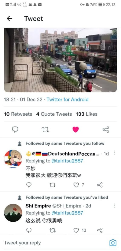 这是一张X（原Twitter）平台的界面截图，顶部是2022年12月1日18:21通过Twitter for Android发布的一条推文，配图为中国台湾地区某街道的实拍画面，能看到临街商铺、行驶的车辆、人行道及远处的居民楼，该推文获得10次转发、4次引用转发、133个点赞。推文下方有两条中文回复：第一条来自昵称带有德国、俄罗斯国旗标识的用户，内容为“不妙 我家很大 歡迎你們來玩w”，获得7个点赞；第二条来自用户Shi Empire，内容为“这么说 你很勇哦”，获得13个点赞。截图顶部还显示了手机状态栏的信号、电量、时间（22:13）等信息。