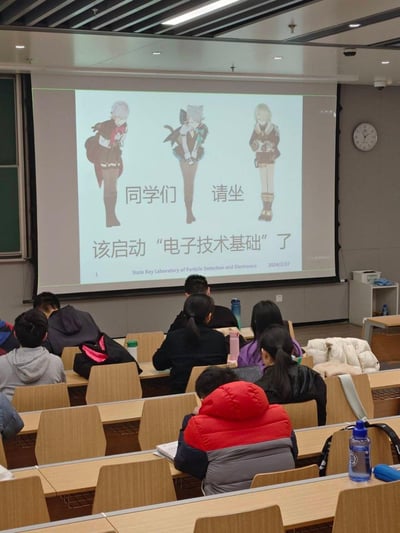 这是在大学教室中拍摄的上课场景，投影屏幕上展示着一份趣味课件封面：使用《原神》中的诺艾尔、琳妮特、菲米尼三位角色的立绘，搭配文字“同学们 请坐 该启动‘电子技术基础’了”，下方标注了粒子探测与电子学国家重点实验室名称及日期2024/2/27。教室里的学生们正坐在座位上准备上课，老师用热门游戏角色制作课件开场，让严肃的专业课程多了几分轻松趣味，图中没有双关、谐音梗等内容。