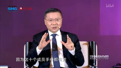 该图是政论节目《这就是中国》的录制片段截图，画面中张维为身着西装佩戴耳麦坐在节目现场的座椅上，双手抬起做出讲解手势，画面下方配字幕“因为这十个成员手中都有货”，画面左上角有上海广播电视台SMG、东方卫视标识，右上角有bilibili标识，右下角有节目《这就是中国》的标识。