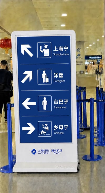 这是一张经过PS恶意修改的虚假图片，冒用上海浦东机场的官方标识，伪造了一块方向指示牌。牌面虚构的分类内容使用了“洋盘”“台巴子”“乡毋宁”等多个带有侮辱性质的地域歧视词汇，还错误地将台湾同胞与中国人并列分类，严重违反一个中国原则，内容十分不当，现实中上海浦东机场从未设置过此类违规指示牌。