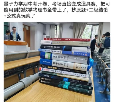 图片展示了大学教室的量子力学开卷考试现场，前景课桌上堆叠着多本厚重的数学和物理教材，包括《量子力学》《数学分析》等。背景中可见几位学生在教室走动，讲台处有老师或学生站立。图片上方配有文字描述考试场景：“量子力学期中考开卷，考场直接变成道具赛，把可能用到的数学物理书全带上了，抄原题+二级结论+公式真玩爽了”，幽默调侃了开卷考试时学生携带大量参考书的夸张状态。