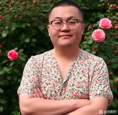 这是一张经过图像合成的搞笑P图，将篮球解说徐静雨的脸部与穿着V领碎花短袖女装的身体拼接在一起。人物双臂交叉抱于胸前，背景是开满粉色玫瑰花的绿植丛。原本具有硬朗气质的男性脸部，搭配温柔风格的碎花女装，形成强烈的视觉反差，整体画风违和又滑稽，通过性别穿搭的反差感制造搞笑效果，图中没有双关、谐音梗或暗示内容。