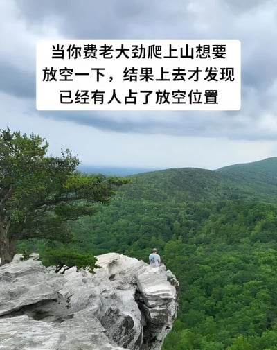 图片展示了一处山顶悬崖景观，悬崖上有一人静坐远眺，背景是连绵的绿色山林和多云的天空。图片上方有白色文字框，内容为“当你费老大劲爬上山想要放空一下，结果上去才发现已经有人占了放空位置”，通过幽默的方式表达了爬山后想独自放松却发现理想位置已被占据的无奈场景。