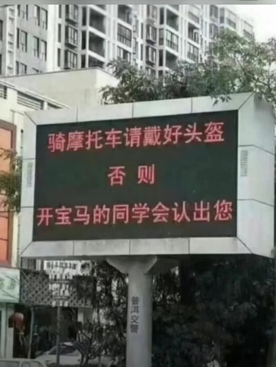 这是一张街头LED电子公告牌，提示“骑摩托车请戴好头盔，否则开宝马的同学会认出您”。本意是安全宣传，却因文案中“宝马同学”梗产生幽默和调侃效果，意外展现阶层、身份与伪装的双关暗示，非常适合用作网络娱乐和自嘲场景。