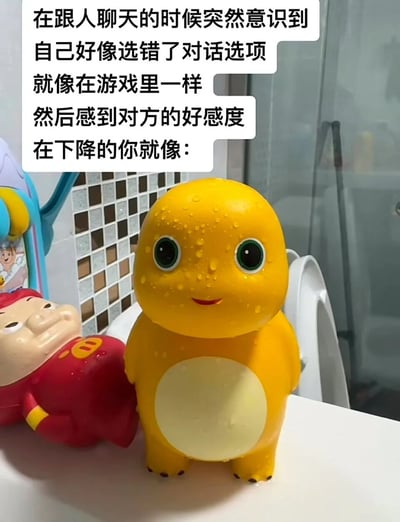 图片展示了一个浴室场景，前景中有两个卡通玩偶：一个黄色的站立玩偶，表面有水珠，表情略带尴尬的微笑；旁边是一个红色的玩偶，呈斜靠姿势，咧嘴笑着。图片上方配有文字，描述了在聊天时突然意识到选错对话选项，感觉像游戏中对方好感度下降时的尴尬心情，黄色玩偶的表情生动呼应了这种情绪。