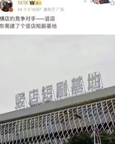 这是一张社交媒体截图，顶部是用户发布的动态内容：“横店的竞争对手——竖店 东莞建了个竖店短剧基地”，下方搭配一张实地拍摄的照片，展示了建筑顶部的“竖店短剧基地”招牌。
图中使用了谐音梗，将知名影视基地“横店”的“横”替换为“竖”，打造出“竖店”这个趣味名称，调侃东莞新建的短剧基地是横店的“反向竞品”，充满幽默趣味。