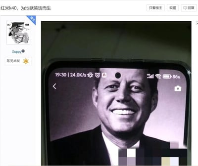这是一张来自国内论坛的帖子截图，帖子标题为“红米k40，为地狱笑话而生”，发布者是名为Guppy的用户，其论坛等级标识为“蒸笼地狱”。帖子核心内容是一张红米K40手机的实拍图，手机屏幕显示着美国前总统约翰·肯尼迪的黑白肖像照，手机的前置单摄像头开孔位置恰好与肯尼迪额头的位置重合，利用肯尼迪遇刺中弹的历史事件，制造出视觉上的黑色幽默（地狱笑话）效果，通过数码产品的设计巧合玩历史相关的梗，属于典型的网络玩梗内容。