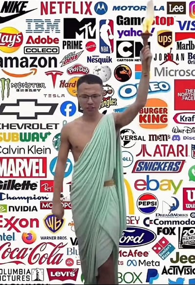 图片中央是一位身着绿色古希腊风格托加袍的男子，右手高举燃烧的火炬，姿态宛如古典雕塑或奥运圣火传递者。背景被数百个全球知名品牌的logo完全覆盖，包括科技巨头（IBM、Microsoft、Amazon）、餐饮品牌（McDonald's、Coca-Cola、Burger King）、运动品牌（Nike、Adidas）、媒体娱乐公司（Netflix、Disney、Warner Bros）等，形成密集的商业符号矩阵。

这种视觉组合形成强烈反差：古典神圣的火炬传递仪式与现代商业品牌的过度饱和形成鲜明对比，暗讽当代社会中商业品牌对公共空间和文化符号的渗透与占领，具有明显的消费主义批判意味。