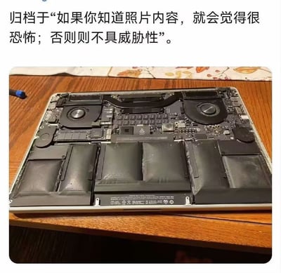 图片展示了一台被拆开后盖的笔记本电脑内部结构，可见多块黑色电池、圆形散热风扇及布满电子元件的电路板，整体放置在带有花纹桌布的木质桌面上。图片上方配有文字：“归档于‘如果你知道照片内容，就会觉得很恐怖；否则则不具威胁性’。” 这种设计通过信息差制造心理悬念——对于了解笔记本电池鼓包风险、电路老化危害等硬件知识的人，可能会联想到设备过热、爆炸等安全隐患，从而产生恐惧感；而对硬件不熟悉的人仅会将其视为普通的电子元件照片。