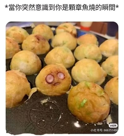 这是一张记录章鱼烧制作过程的实拍图，烤盘里的众多章鱼烧中，有一颗因为嵌入的章鱼粒位置巧合，形成了类似睁大双眼、微张嘴巴的拟人化错愕表情。图片顶部配文“當你突然意識到你是顆章魚燒的瞬間”，用拟人的玩梗方式，赋予这颗章鱼烧“突然觉醒意识到自己是食物”的搞笑设定，充满无厘头的幽默感，让人觉得趣味十足。