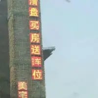 这是一张竖版的实地拍摄照片，画面主体是建筑外墙上的红色发光促销标语，内容为“清盘买房送车位”，下方还有“美宅”字样，是房地产项目进入清盘阶段推出的购房送车位的优惠宣传，以此吸引有购房需求的人群。