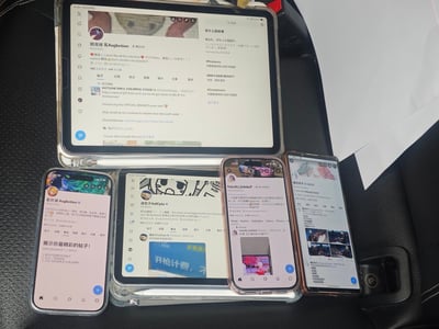这是一张原始拍摄的照片，拍摄场景为汽车的黑色皮质座椅，座椅上摆放了五台电子设备，包括1台大平板电脑、1台小平板电脑和3台智能手机，所有设备的屏幕都打开了X（原Twitter）平台的用户个人主页界面，一共展示了四位不同X用户的主页：最上方的大平板展示“鏡夜綠 寬Augketion”的主页，主页内有一条初音未来相关的活动推广推文；左下方手机同样展示“鏡夜綠 寬Augketion”的主页；中间的小平板展示“迪包子AstCyta”的主页，主页推文可见“开枪计费，不”的中文内容；右中部手机展示原发布者“TekeliLi_iLilekeT”本人的主页；最右侧手机展示“星羽叶子”的主页。这张图是发布者记录线下遇到同平台知名网友（大手子）的分享图。