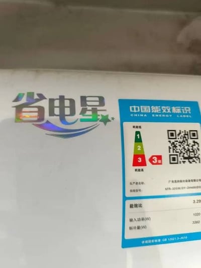 图片为家电产品表面的实拍图，左侧有彩色渐变的“省电星”品牌logo，设计包含蓝色波浪线条和绿色五角星元素；右侧是蓝色底的“中国能效标识”标签，标签内有红黄绿三色能效等级指示（1级最高，图中标识为3级），下方标注了生产者名称、规格型号、能效比（3.29）、输入功率（1020W）、制冷量（3380W）等参数，并附有二维码和依据的国家标准号（GB 12021.3-2010）。整体画面清晰展示了产品的节能标识信息。