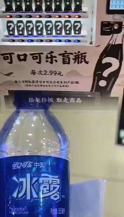 图片展示了一台自动售货机的特写场景。售货机上方货架标注为“可口可乐盲瓶”，售价2.99元/次，宣传语称“每次可随机获得可口可乐公司系列产品1瓶”。货架内商品瓶身均印有问号图案，营造盲选神秘感。图片下方则清晰显示从取货口取出的商品——一瓶蓝色包装的“冰露”饮用纯净水，形成“花2.99元盲盒价买矿泉水”的幽默反差效果。