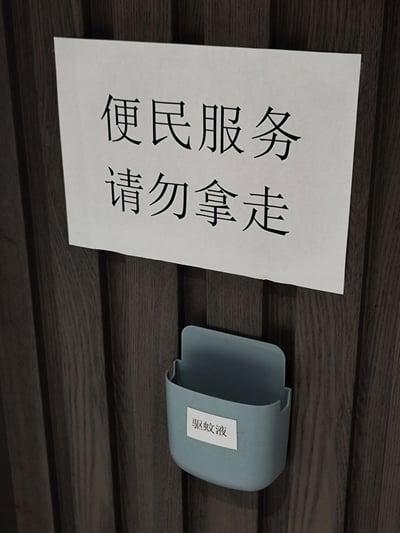这张照片是在公共区域，墙上贴着一张打印的告示：“便民服务 请勿拿走”，下方有一个放置物品的小盒子，贴着“驱蚊液”字样。整体氛围是社区/物业为方便居民免费提供驱蚊液，但也明显担心物品被人带走。告示方式显得有些无奈，容易让人联想到大家“顺手牵羊”的趣事，充满现实幽默感。
双关/暗示：提醒勿拿走其实是担心被“顺走”，表现一种公共物品总被消耗过快的现实无奈。