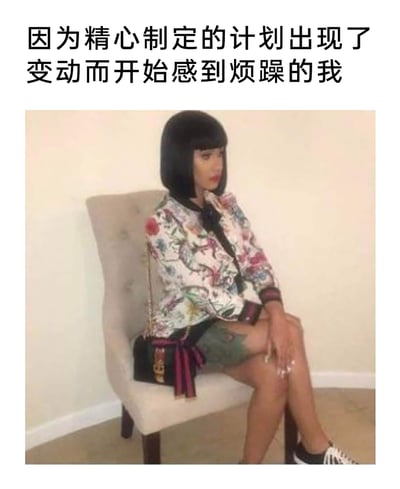 这是一张用来表达情绪的梗图，上方配有文字“因为精心制定的计划出现了变动而开始感到烦躁的我”，图中是美国说唱歌手妮琪·米娜（Nicki Minaj），她坐在浅灰色靠背椅上，身体侧靠，眉头微蹙，神情烦躁低落，一只手搭在腿上，姿态慵懒又郁闷，生动地还原了当自己精心安排的计划被打乱后，那种烦躁、无力又低落的情绪，能够引发很多讨厌计划被变动的人的共鸣。
