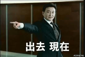 图片中是一位穿着黑色西装的男性，表情愤怒严肃，右手伸出食指指向前方，背景为深色木质墙面，整体场景像是在办公室或正式场合。图片下方有白色大字文本“出去 现在”，表达强烈的驱赶意图，常用于网络中模拟愤怒呵斥、驱赶他人的场景。