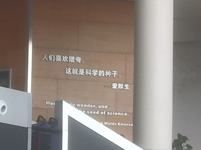照片展示了一面写有中英双语励志名言的墙，内容为爱默生的“人们喜欢猎奇，这就是科学的种子”，中英文对照陈列，表达了好奇心对科学发展的重要性。环境看起来像是学校、科技馆或类似的公共学习空间，充满学习氛围，非常适合用来激励青少年发掘科学兴趣。

暂无发现谐音梗、双关、暗示或网络流行语。