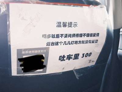 这是一张拍摄于烟台出租车（或网约车）后座的趣味提示贴纸，贴纸以接地气的本土调侃口吻撰写：
1. 温馨提示：喝多以后不要问师傅相不相信爱情，烟台这个几儿灯地方就没有爱情
2. 明确收费规则：吐车里 300
3. 附带推荐使用微信支付的标识
整体风格搞笑又硬核，用自嘲式的本地吐槽，既提醒醉酒乘客避免尴尬提问，又清晰告知违规收费标准，充满烟火气的幽默很容易引发共鸣。