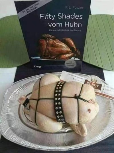 图片中展示了一只生鸡肉被黑色绳索和带钉皮带捆绑在铝箔托盘上，前方摆放着一本德语食谱书《Fifty Shades vom Huhn》（《五十度鸡》）。该书封面印有烤鸡图案，明显恶搞了畅销情色小说《五十度灰》（Fifty Shades of Grey），将情欲主题与烹饪幽默结合。生鸡肉的捆绑方式模仿了BDSM元素，与食谱书的“情色烹饪”副标题形成荒诞对比，营造出滑稽效果。