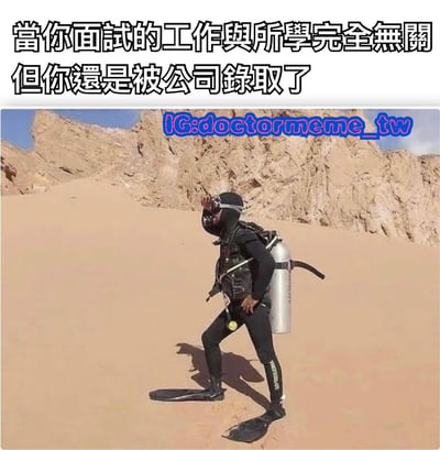 图片上方配有文字‘當你面試的工作與所學完全無關但你還是被公司錄取了’，下方是一名穿着全套潜水装备（包括潜水服、氧气瓶、脚蹼）的人站在沙漠中，背景是荒凉的沙丘和岩石山脉。通过潜水装备与沙漠环境的强烈反差，幽默地表达了‘所学与工作无关却被录用’的荒诞感和无奈情绪。