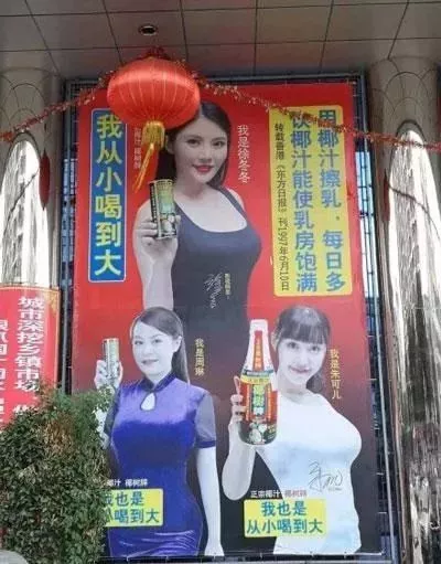 图片展示了一幅大型户外广告海报，背景为鲜艳红色，上方悬挂红色灯笼并装饰彩带。海报中包含三位女性模特，分别手持罐装和瓶装椰汁产品，表情自然微笑。广告文字内容包括左侧竖排的'我从小喝到大'，右侧黄色背景文字'用椰汁擦乳，每日多饮椰汁使乳房饱满'，以及底部两位模特旁的'我也是从小喝到大'标语。因宣传语涉及性暗示引发公众争议，是具有话题性的商业广告案例。