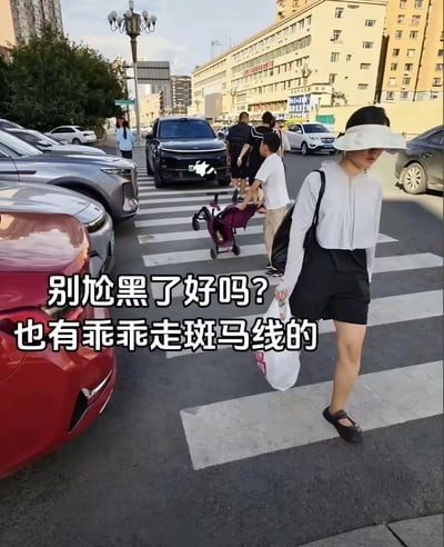 这是一张城市斑马线处的实拍图，画面中有多位行人正在通过斑马线，其中小男孩推婴儿车的场景形成了视觉错位，看起来仿佛是“婴儿”在推车，产生有趣的反差感；配文“别尬黑了好吗？也有乖乖走斑马线的”，像是在回应外界对行人不遵守交通规则的批评，用该画面证明存在遵守规则的行人，视觉错位的细节也为内容增添了搞笑氛围。