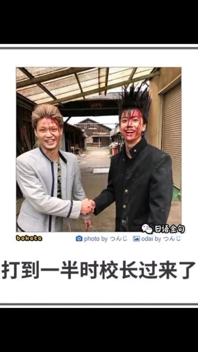 这是一张基于日剧《我是大哥大》画面制作的搞笑梗图，图中是剧中主角三桥贵志与伊藤真司的演员真人画面，两人脸上布满打斗后的血迹，却摆出友好握手的姿势，脸上洋溢着夸张的大笑表情，下方配文“打到一半时校长过来了”。该图通过不良少年打架中途撞见校长，立刻从敌对状态切换为和睦友好的强烈反差感，制造出滑稽搞笑的效果，精准还原了校园场景里那种尴尬又好笑的突发状况，引发网友对类似经历的共鸣。