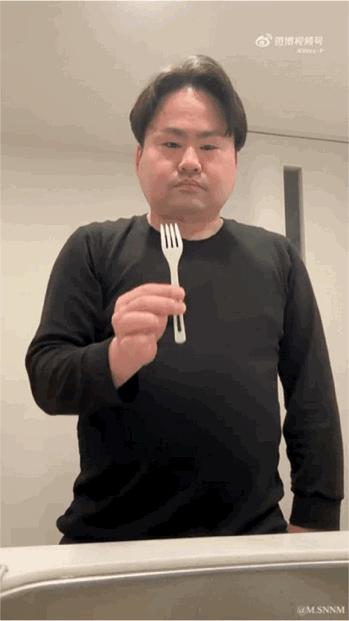 这是一个趣味视觉错位动态GIF，画面中一位身着黑色上衣的真人男性，手持一把白色塑料叉子，通过拍摄角度的巧妙设计，让叉子看起来仿佛产生了伸缩的视觉错觉，男性全程表情严肃，和搞笑的视觉效果形成反差，带来诙谐的观看体验。
没有双关、谐音梗或暗示内容，仅靠视觉错位制造趣味。