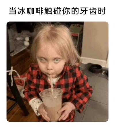 这是一张搞笑梗图，顶部配有文字“当冰咖啡触碰你的牙齿时”，图中是一位穿着红黑格子睡衣的金发小女孩，双手捧着一杯冰咖啡，正用吸管饮用，同时她的眼睛向上翻起，面部神情生动地还原了人们饮用冰饮时，冰感刺激牙齿所产生的那种酸爽、难受又略带上头的体验，用夸张的表情精准戳中了很多人喝冰饮时的真实感受，充满趣味性。