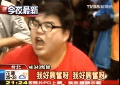 这是一张TVBS新闻台的视频截图，画面中是一位身穿红色上衣的AKB48男性粉丝，他戴着眼镜，表情极度兴奋，正张嘴大喊。屏幕上方有“今夜最新”和“TVBS新聞台”的标识，下方字幕显示“台北 AKB48粉絲 我好興奮呀 我好興奮呀”，左下角还有花莲天气“25-28℃”及时间“21:24”的信息。