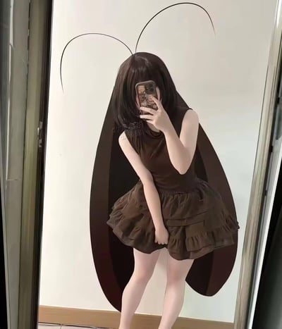图中女生穿着深棕色无袖蓬蓬裙，手持带卡通图案的手机对着镜子自拍，通过后期修图添加了蟑螂的黑色触须和翅膀，将自己装扮成拟人化的蟑螂娘，可爱的穿搭和蟑螂元素形成强烈反差，打造出搞怪有趣的效果。
