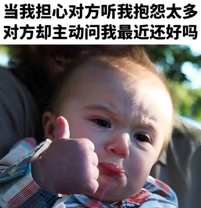 图片上方有文字“当我担心对方听我抱怨太多 对方却主动问我最近还好吗”，下方是一个婴儿的特写照片。婴儿穿着彩色条纹衬衫，正竖起大拇指，脸上带着略带委屈又感动的表情。背景是模糊的户外绿色植物，营造出温暖的氛围。