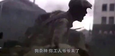 这是一张影视剧截图，画面主体是一位戴着鸭舌帽、身着工装的男性工人角色，他身体前倾，面部朝向画面右侧，嘴巴大张，正处于愤怒呐喊的状态，情绪十分激动。画面下方配有白色的台词字幕“狗杂种 你工人爷爷来了”，直白地传递出角色的愤怒与敌视情绪。背景是模糊的建筑物，整体场景看起来像是在一个充满冲突的工业或战斗环境中，营造出紧张激烈的氛围。
