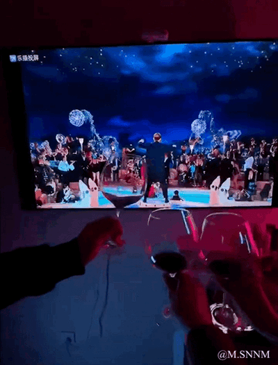 这张图是网友的创意拍摄：现实中几个人举着红酒杯，对着正在播放经典电影《泰坦尼克号》的电视屏幕举杯，屏幕里是杰克赢得船票后参加头等舱晚宴、被众人簇拥的热闹名场面。通过这种同步动作，把现实观影场景和影视内容结合，营造出仿佛置身电影舞会的沉浸式趣味氛围，充满欢乐感。