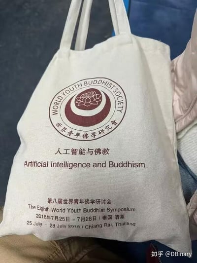 这是一张展示第八届世界青年佛学研讨会主题帆布包的静态实拍图，包身为米白色帆布材质。包身顶部印有世界青年佛学研究会的圆形标志，标志中心是莲花图案，外圈环绕着中英文的研究会名称；标志下方是研讨会的核心主题“人工智能与佛教”及对应的英文翻译；再往下依次是第八届世界青年佛学研讨会的中英文全称、举办时间“2018年7月25日-7月28日”与举办地点“泰国清莱”的中英双语信息。图片右下角带有知乎用户@DBinary的水印，整体风格正式，体现了传统佛学研究与现代科技议题结合的学术研讨方向，是该研讨会的官方周边物品。