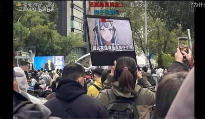 这是一张B站视频的截图，记录了街头抗议活动的现场：人群中一位女生举着一块自制标语牌，牌面是表情略显无奈的二次元动漫少女，配文“国民党還真是高高在上呢”，用诙谐的二次元梗图形式表达对国民党的不满。画面上方的B站弹幕也玩起了梗，出现“祥子说得对”“还真是高高在上 要笑死了”“绷......”等内容，将严肃的抗议场景和二次元文化结合，增添了讽刺又搞笑的氛围。