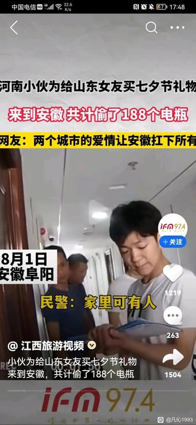 这是一段新闻视频的竖屏截图，内容为8月1日安徽阜阳警方抓获一名盗窃电瓶的河南小伙，该男子称是为了给山东女友买七夕节礼物，共计偷了188个电瓶。图中配文和网友评论玩起地域梗：“两个城市的爱情让安徽扛下所有”，将违法盗窃事件用跨地域的反差感进行调侃，民警在现场询问男子“家里可有人”，男子低头面露羞愧，双手被约束。整体内容充满荒诞搞笑的反差感，把盗窃行为和“爱情”绑定，用地域梗制造笑点。