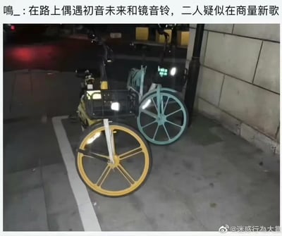 图片展示了两辆停放在夜间路边的共享单车，一辆车轮为黄色，另一辆为蓝绿色。图片上方配有文字“呜_：在路上偶遇初音未来和镜音铃，二人疑似在商量新歌”，通过共享单车的颜色（初音未来常关联绿色，镜音铃常关联黄色）幽默地将车辆比作两位虚拟歌手，制造出“偶遇虚拟歌手骑共享单车商量新歌”的迷惑又搞笑的效果。图片右下角有水印“@迷惑行为大赏”。