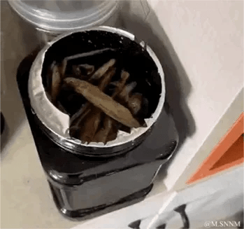 这是一张充满趣味的视觉错位照片，画面中原本是装有干制小鱼的黑色罐子，由于拍摄角度和罐子的金属边缘的巧合，让整个罐子看起来像是一张张开的嘴，罐内的干制小鱼仿佛是舌头，形成了极具迷惑性的视觉错觉，让人第一眼产生误解，带来搞笑的观感。
