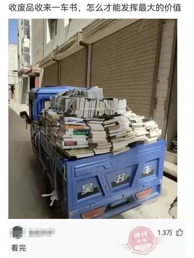 图片中一辆蓝色卡车的车厢里堆满了各式各样的书籍，书籍堆叠得较高且用绳子简单固定，涵盖不同厚度和颜色的读物。卡车停在一条狭窄的巷弄内，两侧是灰白色的建筑物，墙面略显斑驳，旁边是紧闭的卷帘门商铺。图片顶部配有文字“收废品收来一车书，怎么才能发挥最大的价值”，引发对这些回收书籍如何实现价值最大化的思考。整体场景呈现出日常生活中废品回收的真实画面，充满生活气息与实用疑问。