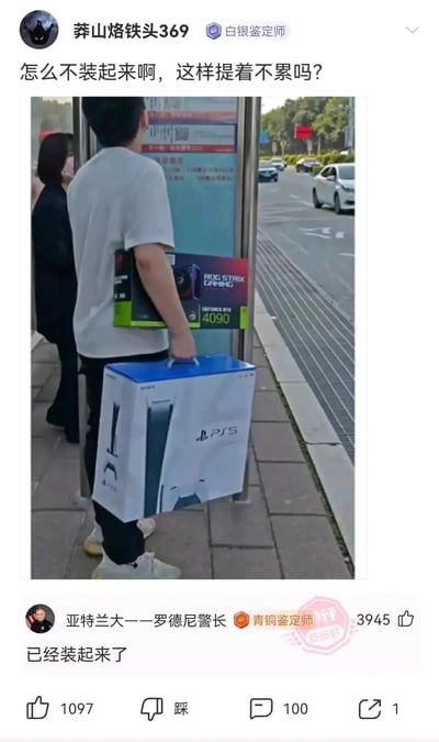 这是一张来自皮皮虾平台的社交媒体截图，画面呈现的是城市户外公交站场景：一名穿浅色短袖的男子站在站台边缘，左臂夹着一个ROG STRIX GAMING系列的GeForce RTX 4090高端显卡包装盒，右手则提着一个索尼PS5游戏机的大包装盒，旁边还有一名女子站在站台处。发布者“莽山烙铁头369”配文提问“怎么不装起来啊，这样提着不累吗？”，用户“亚特兰大——罗德尼警长”的评论“已经装起来了”成为笑点，这里运用了双关梗：表面是质疑没把显卡放进PS5盒子里，实际是调侃当前高端显卡价格高昂，玩家投入大量资金购买显卡后，PS5的价值相对显得较低，只能被当作“装显卡的容器”，形成了数码产品价值反差的搞笑效果，戳中了数码爱好者圈子里关于高端硬件价格的共鸣点。