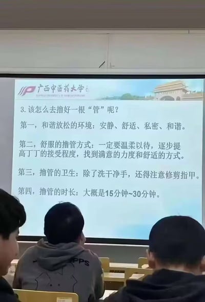 这是一张高校教室的实拍照片，画面主体是前方投影幕布上显示的广西中医药大学课程PPT，PPT内容围绕“撸好一根管”列出四点操作注意事项，用词“撸管”“丁丁”极易和低俗俚语产生谐音联想，引发歧义。画面下方可见三名坐在座位上的学生，其中左侧一名学生仅露出半张脸，面带笑意，另外两名学生背对镜头看向投影方向。