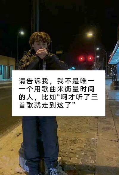 这是一张实拍的夜晚城市街道静态图，画面中一位卷发、身着深色外套的人站在路边的金属柱子上，双手抬至嘴边，低头的神态带有一丝感慨，背景是亮着暖黄色路灯和红色交通信号灯的静谧街道，两侧是临街店铺。图片中间叠加了一个白色文字框，框内的文字是一段能引发大众共鸣的日常感慨：“请告诉我，我不是唯一一个用歌曲来衡量时间的人，比如"啊才听了三首歌就走到这了"”，精准描述了很多人在步行、通勤时，习惯以播放歌曲的数量来感知时间流逝和路程进度的生活小细节，容易让有相同习惯的人产生认同。