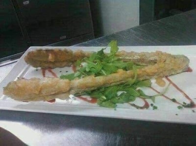 这是一张构图清晰的实拍美食照片，白色长形餐盘内摆放着两段经过油炸处理的食物，其外形高度酷似人类的小腿，容易让人产生视觉错觉；餐盘中间搭配了新鲜绿色叶菜作为点缀，盘底还绘制了红色与浅棕色的酱汁线条来做装饰，整体摆盘精致，因食物的特殊外形充满了趣味与猎奇感。