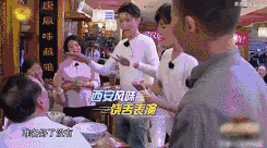 这是一张户外综艺的录制现场截图，场景位于西安的一家风味餐馆内，几名身着浅色统一服装的综艺成员正在和身边的人互动。画面中间的成员正抬手对着对面的人说话，表情带着恳求感，画面配有字幕“西安风味 一段苦表演”，左下角还有该成员的台词“都给你表演了啊”，背景中能看到餐馆的其他食客，整体氛围轻松，呈现出综艺里成员为完成任务进行表演的趣味场景。